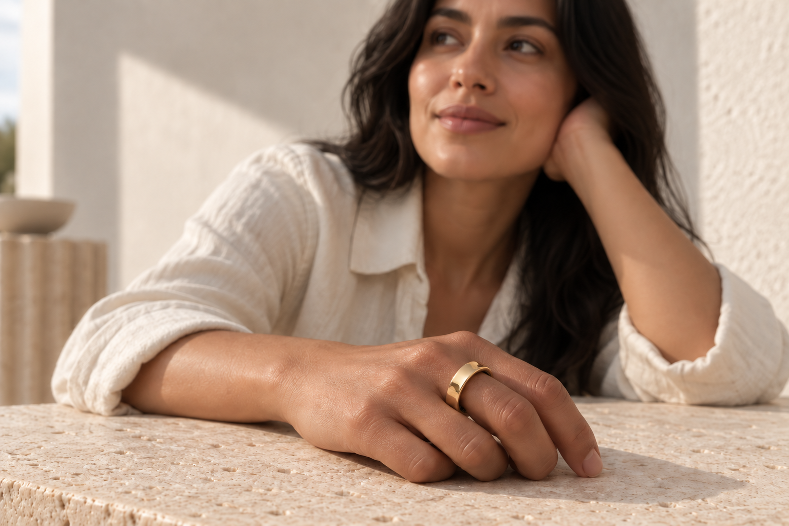 Woman wearing a gold Rune 1 smart ring, her hand resting on sunlit stone.